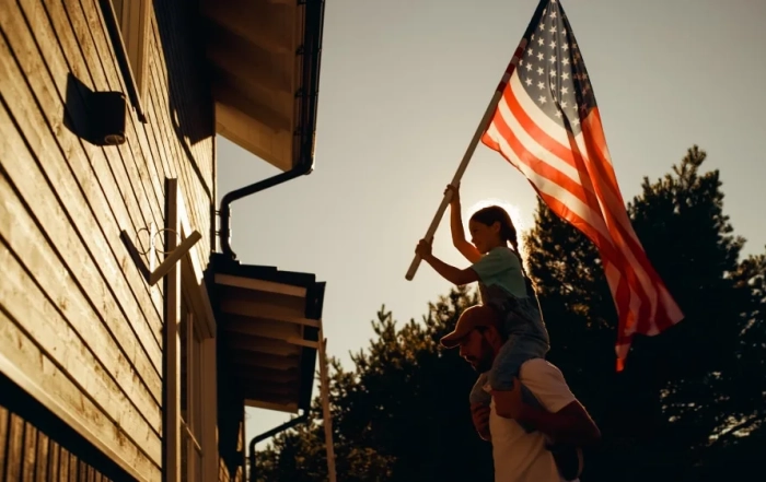 a little girl holding a large american flag while sitting on her fathers shoulders